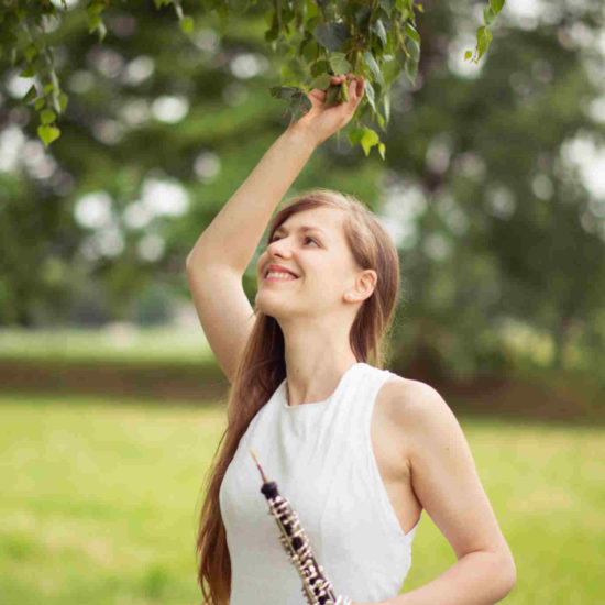 Die Dresdner Musikerin Elisabeth Beckert greift in einem weißen Kleid nach einem Zweig und hält in der anderen Hand eine Oboe