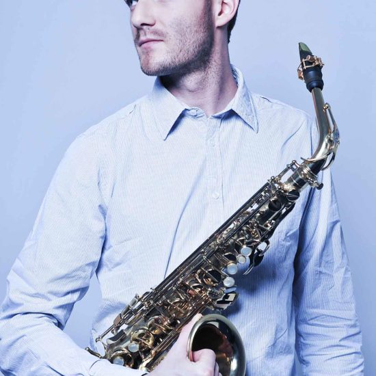 Der Saxophonist Richard Ebert hält sein Saxophon in der Hand und schaut zur Seite